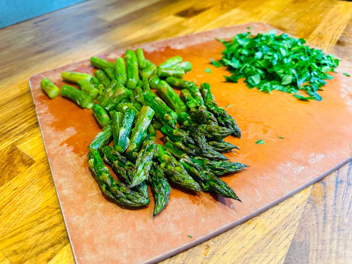 Chopped roasted asparagus and chopped parsley on a cutting board.