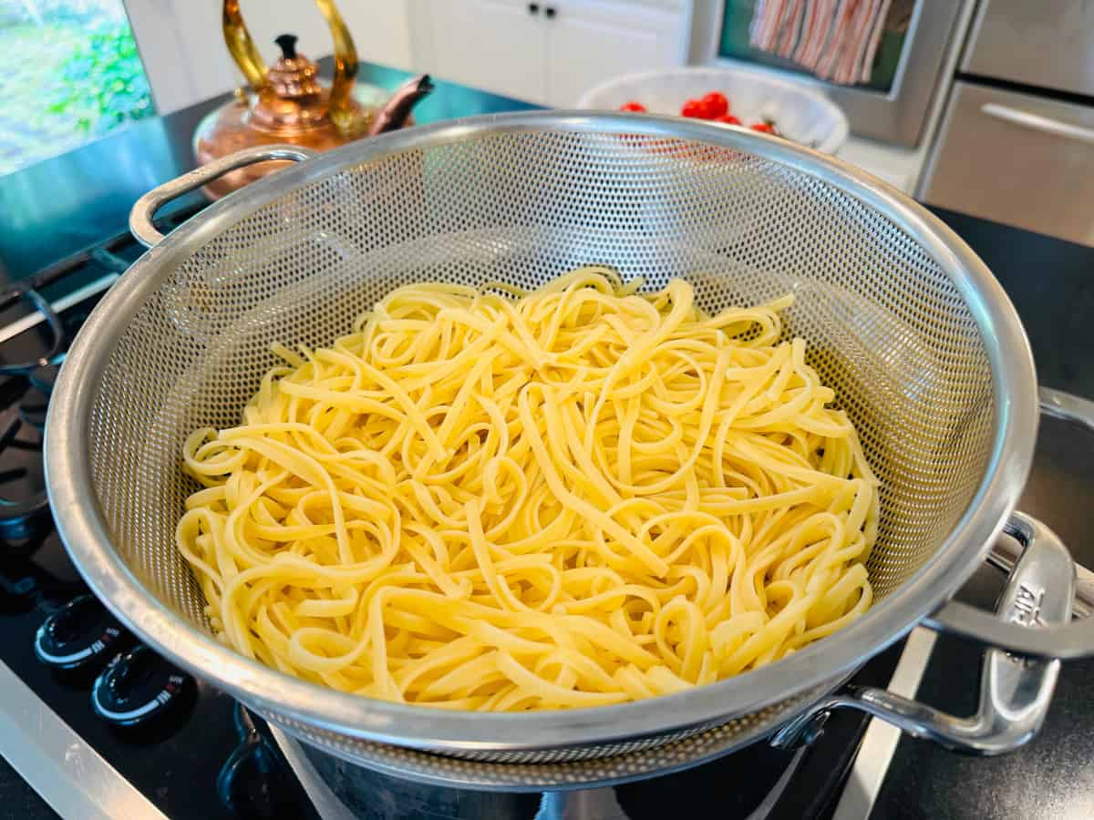 Cooked linguine in a colander sitting on top of a large steel pot.