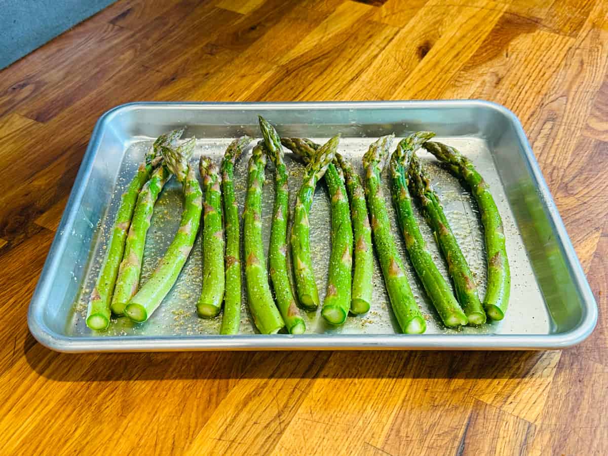 Asparagus spears covered in olive oil and sprinkled with salt and pepper on a small metal baking sheet.