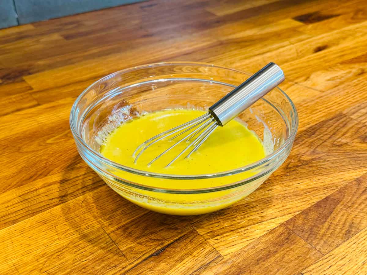 Yellow liquid in a small glass bowl with a little steel whisk.