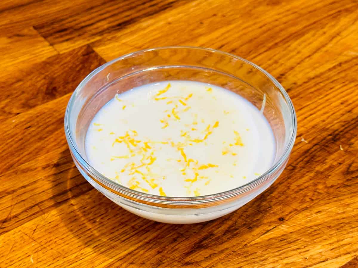Lemon zest sprinkled into a small glass bowl of milk.