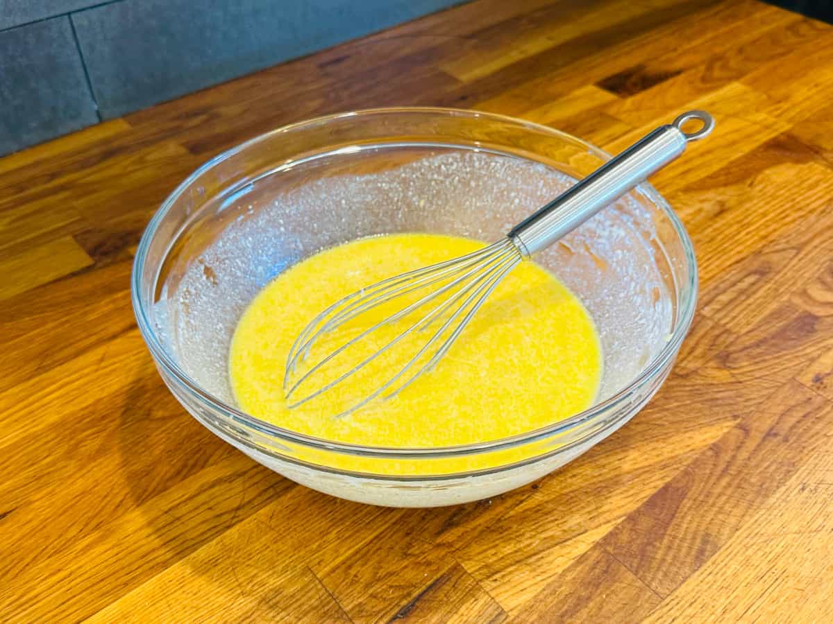 Yellow liquid in a glass bowl with a steel whisk.