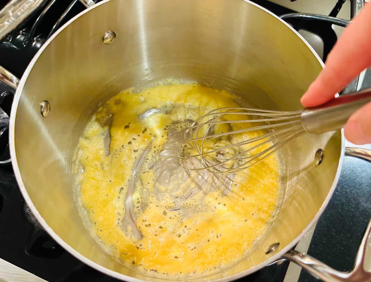 Foamy pale yellow mixture being whisked in the bottom of a steel saucepan.
