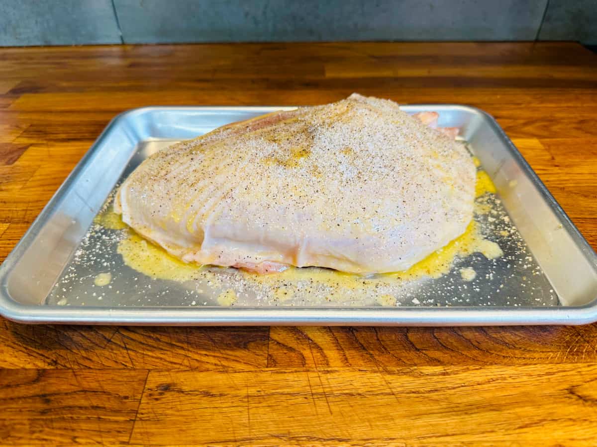 Raw turkey breast brushed with melted butter and sprinkled with salt and pepper on a metal half baking sheet.