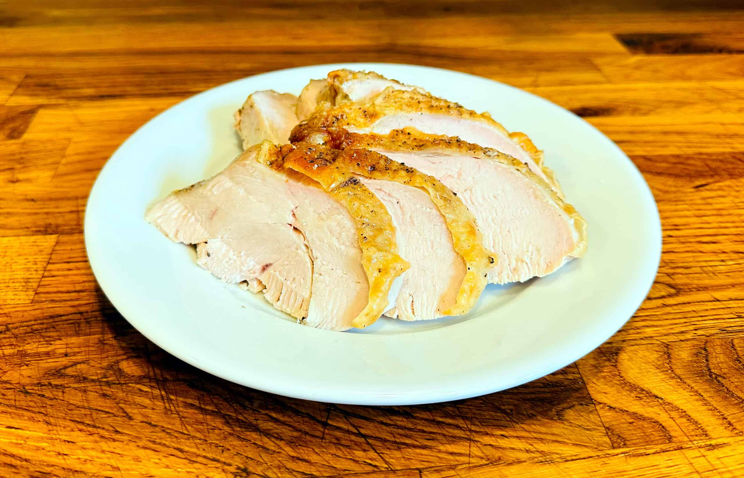Sliced roasted turkey breast fanned out on a white plate sitting on a wood countertop.
