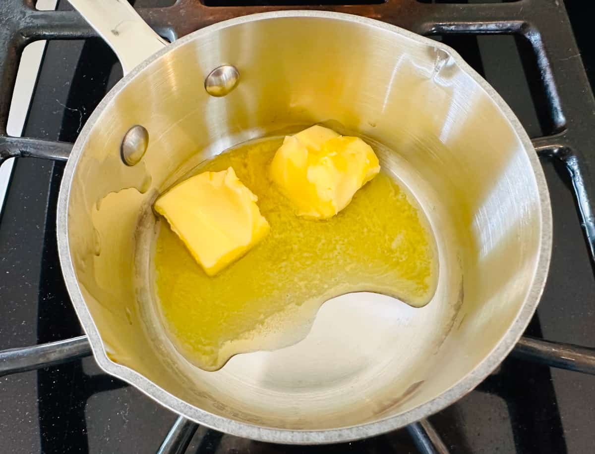 Two cubes of butter melting in a small steel saucepan on the stove.