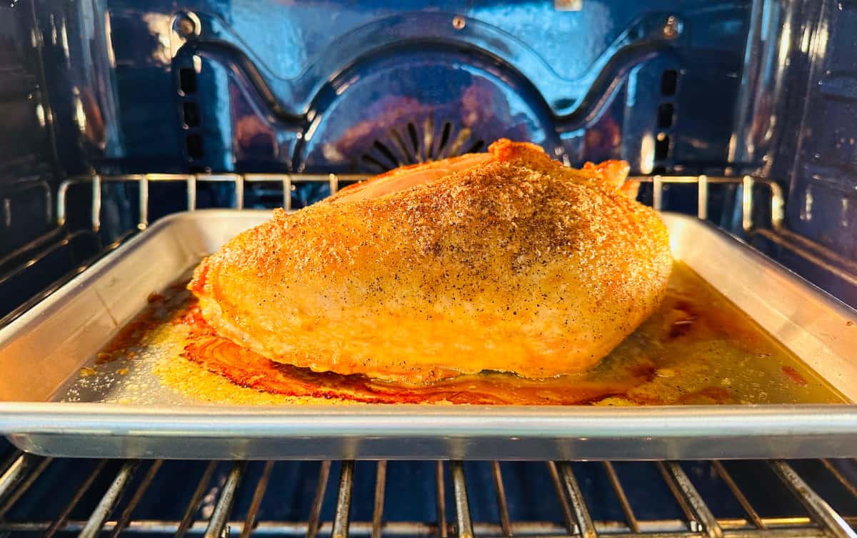 Turkey breast roasting on a metal half baking sheet in a blue oven.