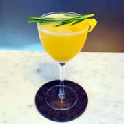 Rosemary lemon drop cocktail in a coupe glass with a sprig of fresh rosemary and a lemon twist.