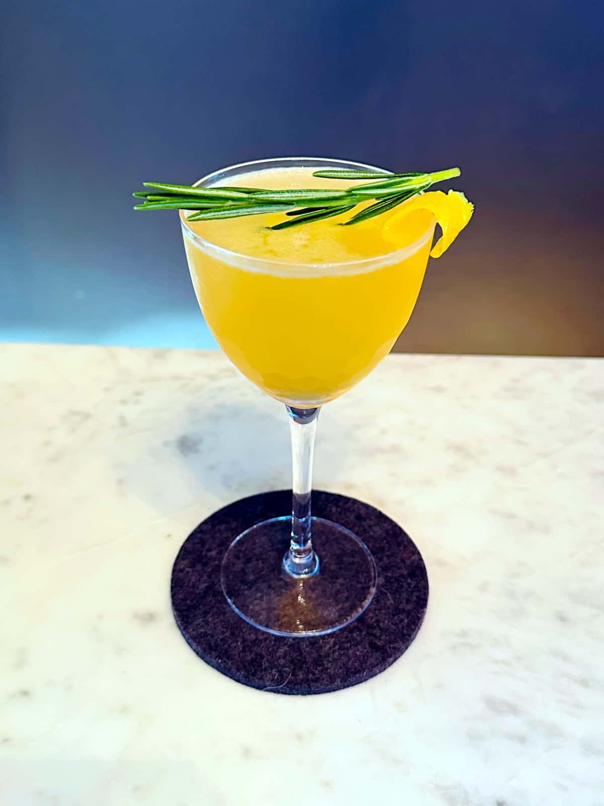 Rosemary lemon drop cocktail in a coupe glass with a sprig of fresh rosemary and a lemon twist.