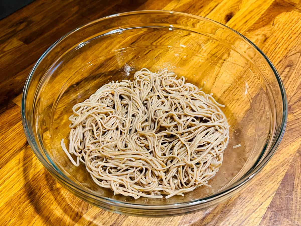 Soba noodles coated with dressing in a large glass bowl.