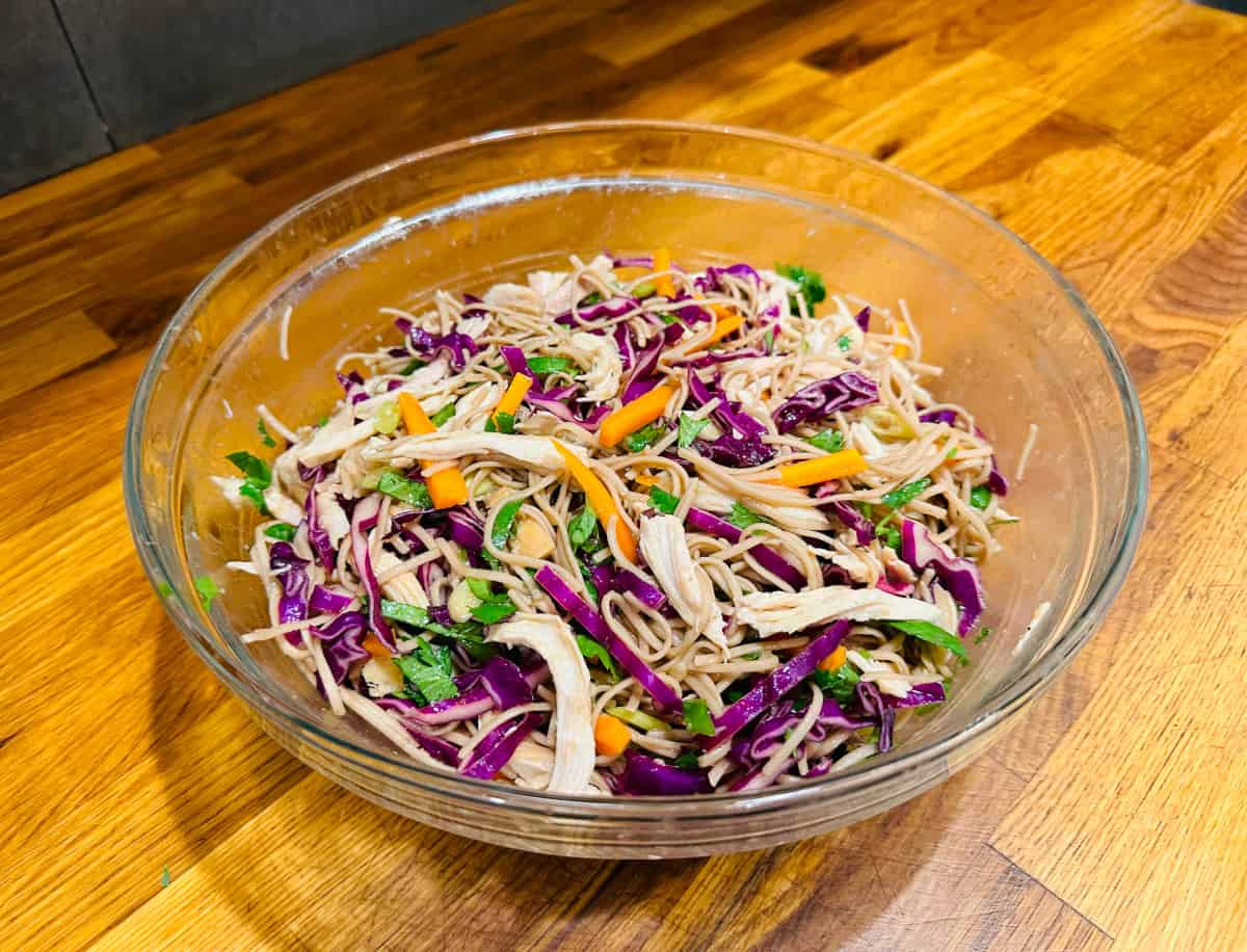 Soba noodles, red cabbage, carrots, scallions, cilantro, and chicken tossed together in a glass bowl.
