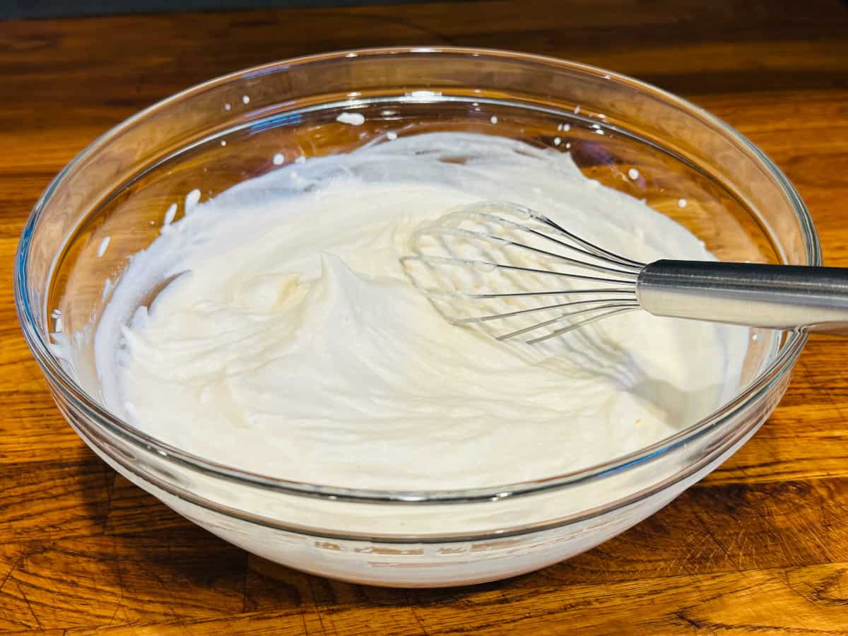Billowy white cream in a glass bowl with a metal whisk.