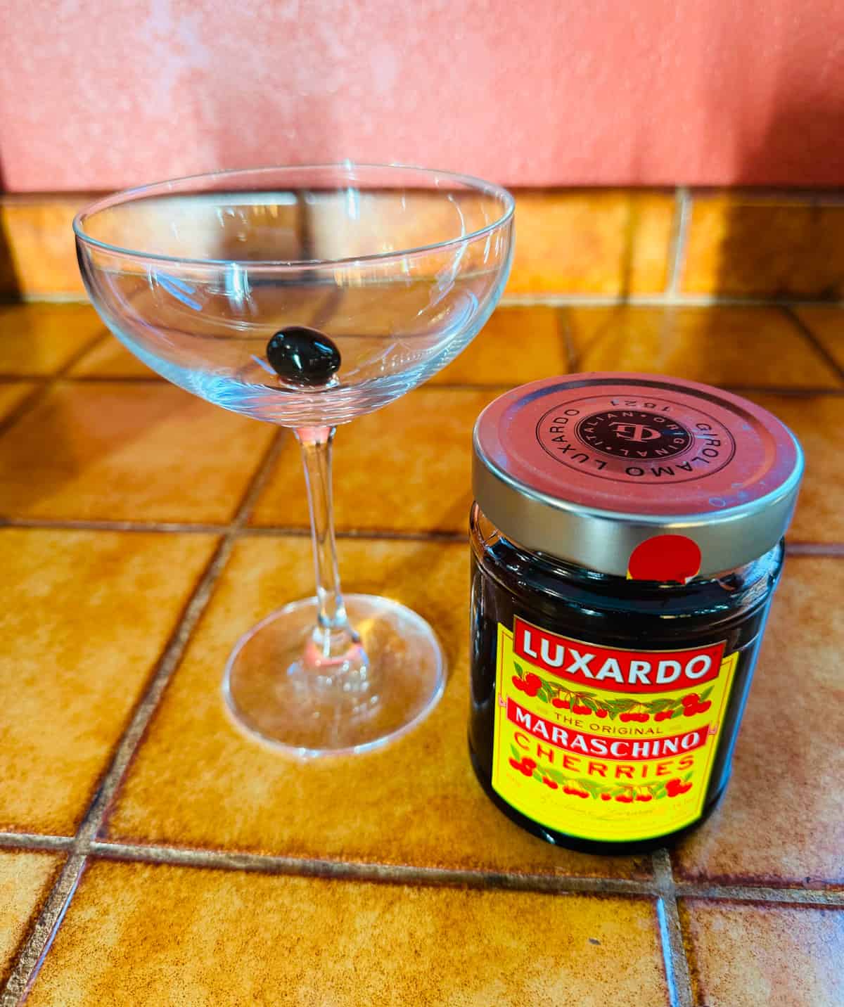 Coupe glass with a maraschino cherry in the bottom next to a jar of luxardo cherries.
