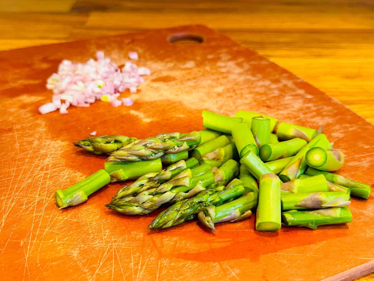 Chopped asparagus and shallot on a cutting board.