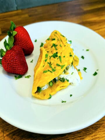 Asparagus omelette sprinkled with parsley on a white plate with two large strawberries.