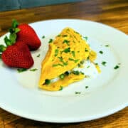 Asparagus omelette sprinkled with parsley on a white plate with two large strawberries.