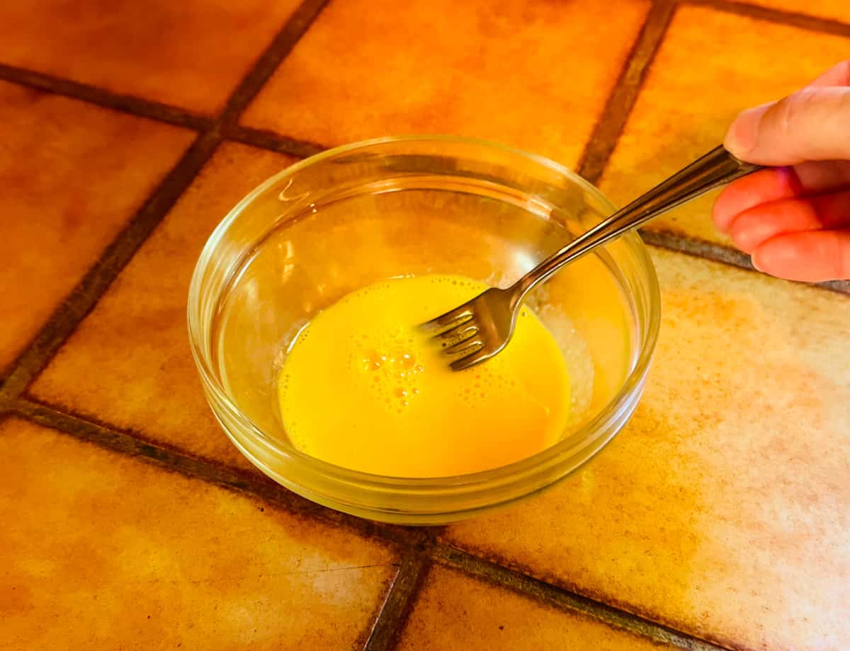 Egg being beaten with a fork in a small glass bowl.