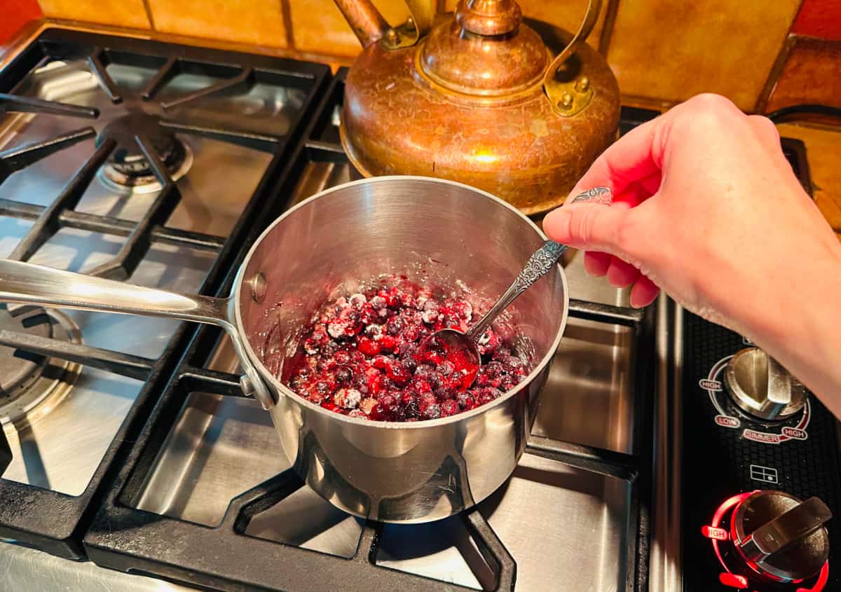 Blueberry filling ingredients being stirred in a small steel saucepan on the stove.
