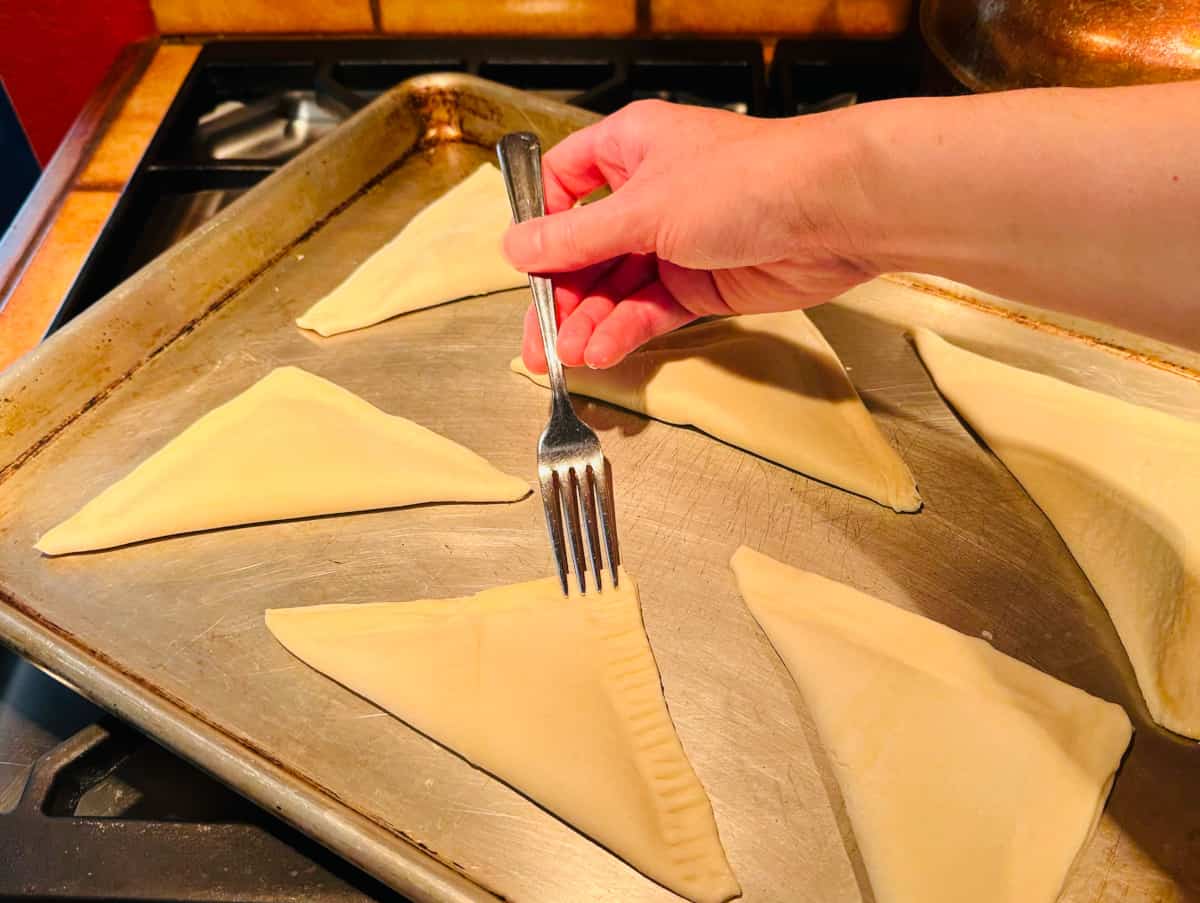 Turnovers on a metal baking sheet being pressed along the edges with a fork.