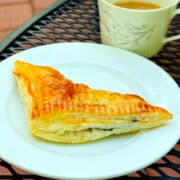 Blueberry turnover on a small white plate next to a cup of coffee.