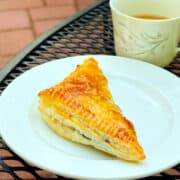 Blueberry turnover on a white plate with a cup of coffee alongside sitting on an black metal outdoor table.