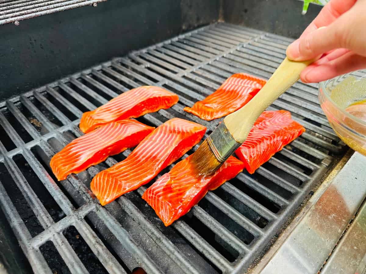 Glaze being brushed onto salmon pieces cooking on a gas grill.