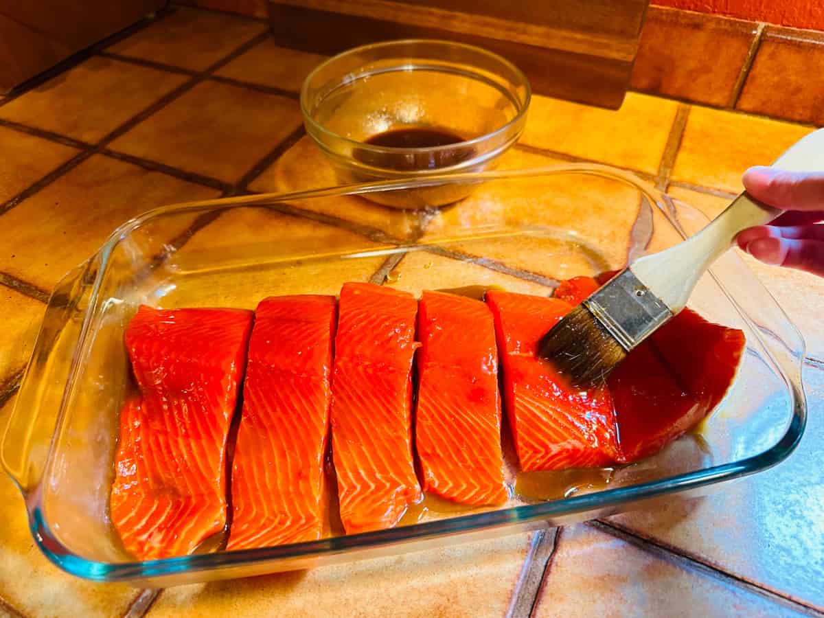 Glaze being brushed onto salmon pieces in a glass dish.