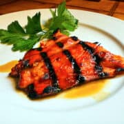 Glazed salmon and a sprig of parsley on a white plate.