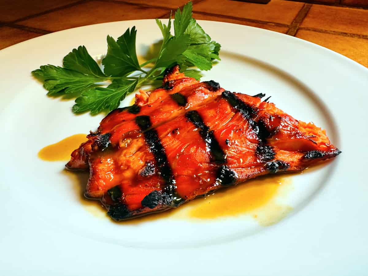 Glazed salmon and a sprig of parsley on a white plate.