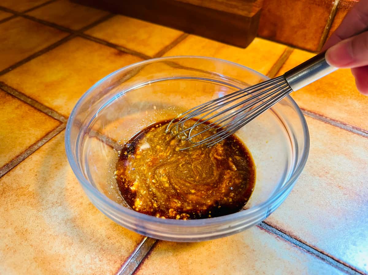 Shoyu, mustard, and dark brown sugar being whisked together in a small glass bowl.