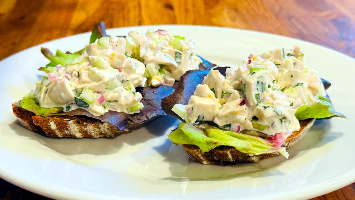 Tarragon chicken salad and lettuce on two slices of dark bread sitting on a white plate.
