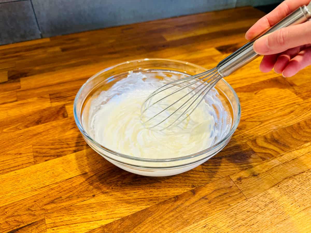 White creamy mixture being whisked in a glass bowl.