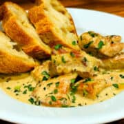 Chicken tarragon and three small slices of crusty bread in a shallow white bowl.
