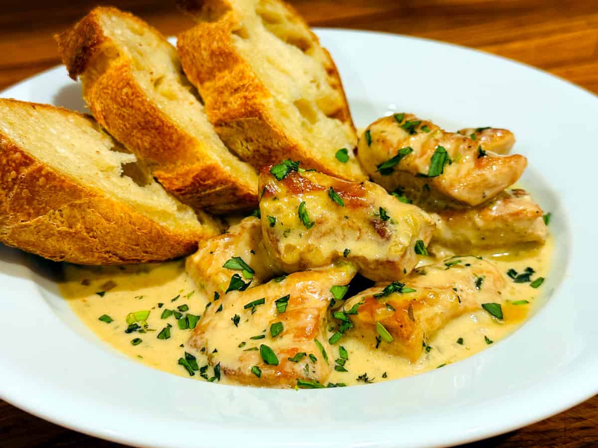 Chicken tarragon and three small slices of crusty bread in a shallow white bowl.