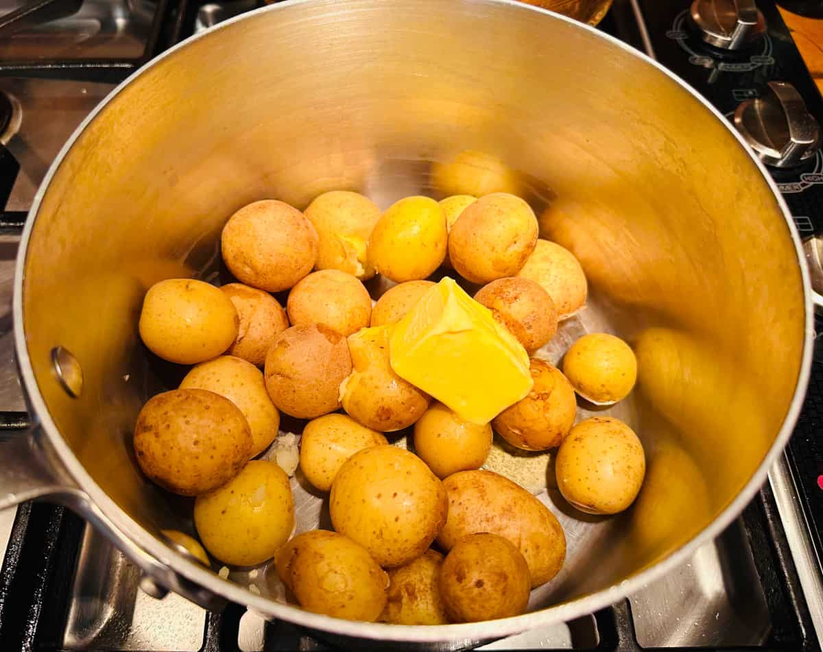 Small yellow potatoes with a big chunk of butter in a large steel saucepan.