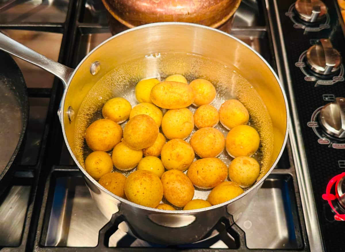 Small whole yellow potatoes covered in water in a large saucepan sitting on the stove.