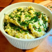 French country mashed potatoes garnished with chopped chives in a round white serving dish.