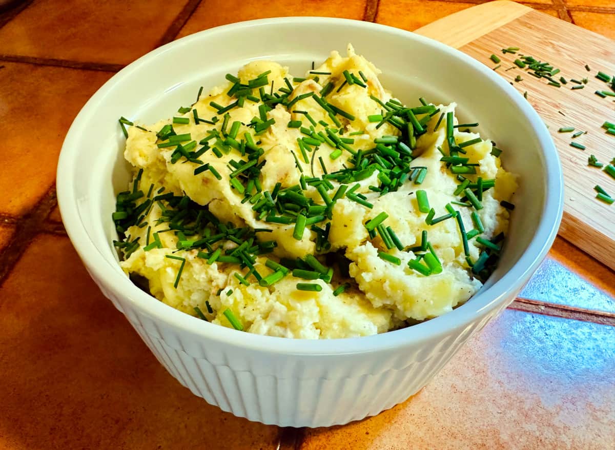 French country mashed potatoes garnished with chopped chives in a round white serving dish.