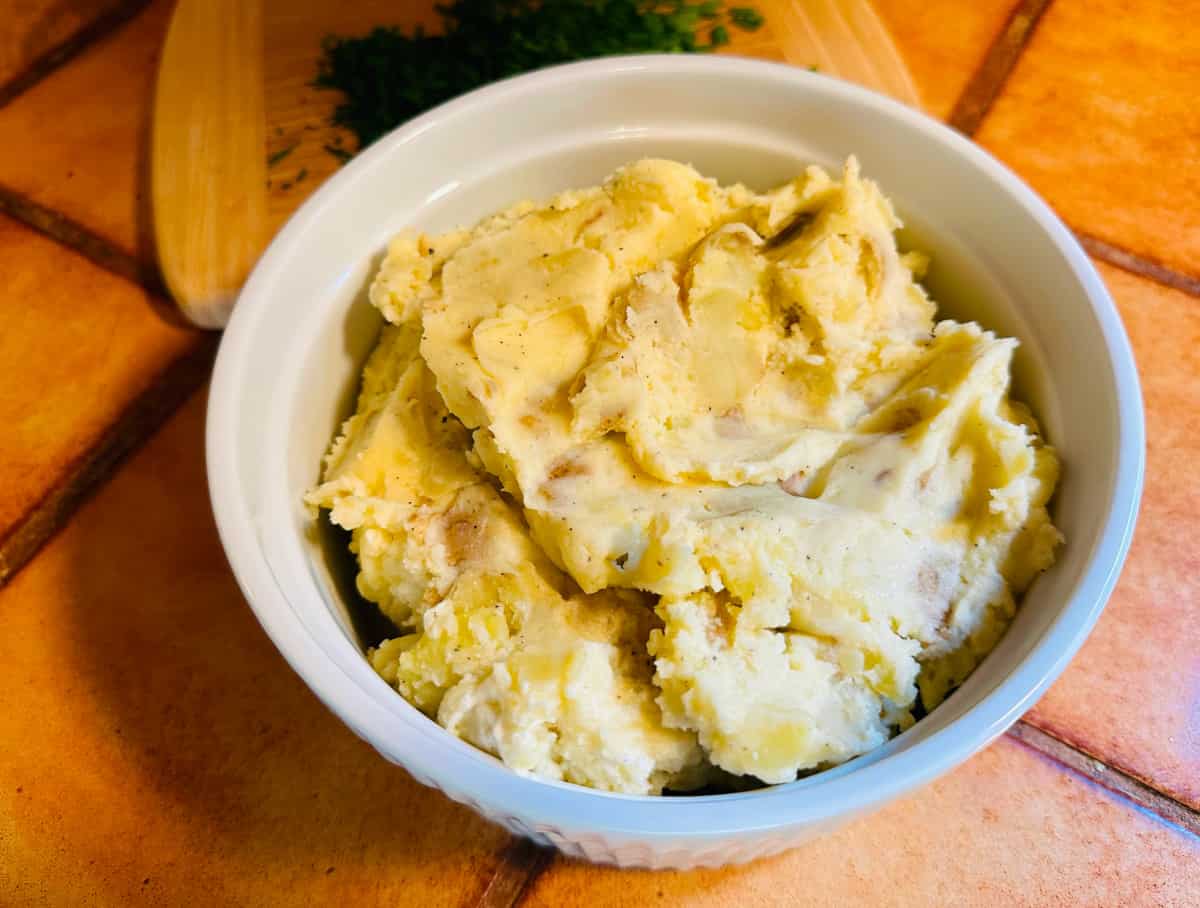 Roughly mashed potatoes in a round white serving dish.