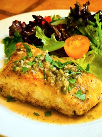 Halibut piccata in front of a green salad on a white plate.