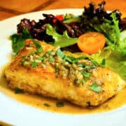 Halibut piccata in front of a green salad on a white plate.