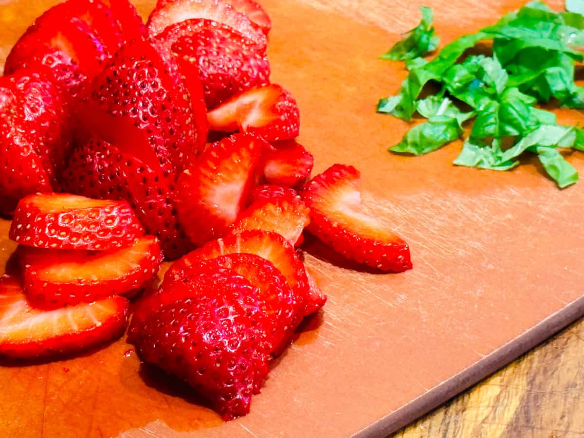 Sliced strawberries and chopped basil on a cutting board.
