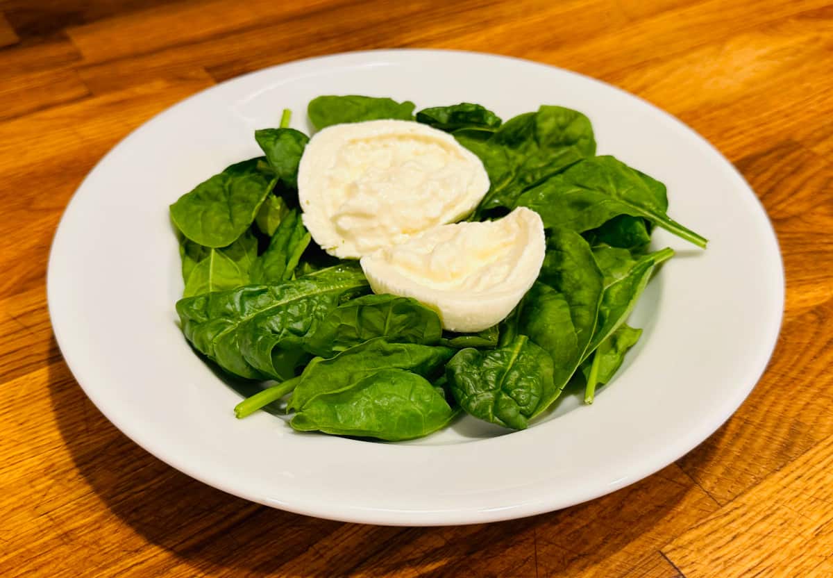 Two burrata ball halves sitting on a bed of spinach in a shallow white bowl.