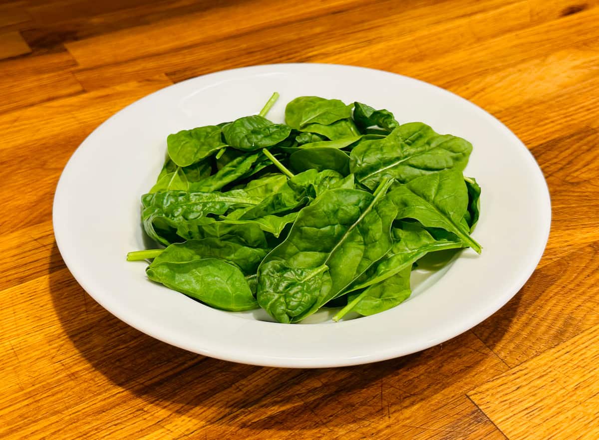 Spinach strewn across the bottom of a shallow white bowl.