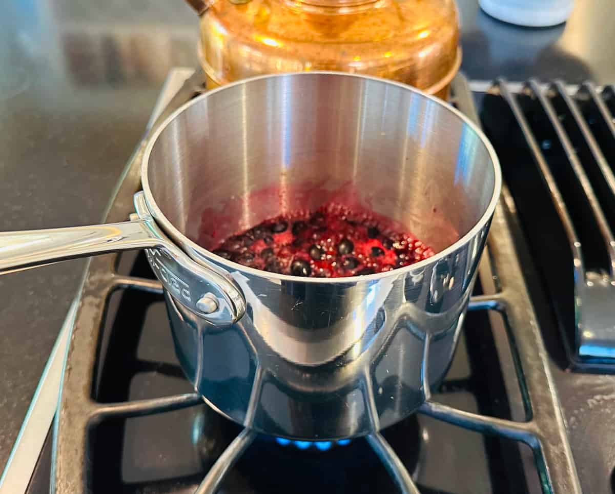 Blueberry compote simmering in a small steel saucepan on the stove.