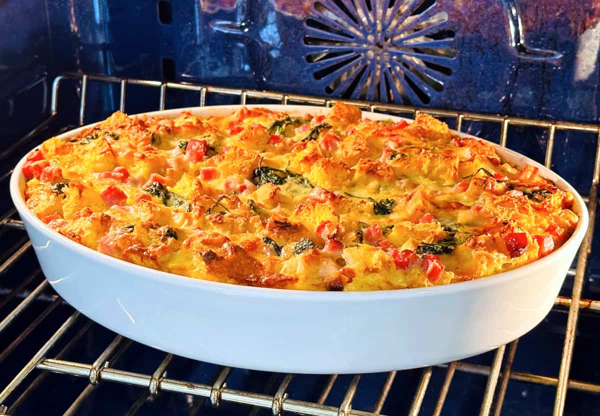 Breakfast strata in an oval white dish baking in a blue oven.