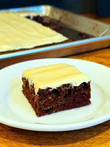Chocolate zucchini bar topped with cream cheese frosting on a small white plate.