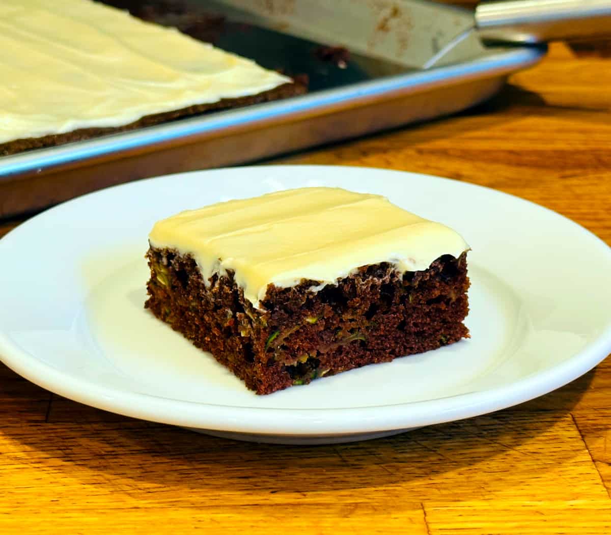 Chocolate zucchini bar topped with cream cheese frosting on a small white plate.