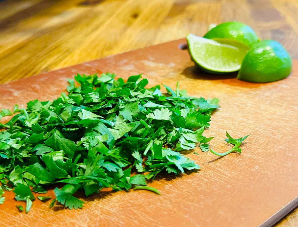 Chopped cilantro and a quartered lime on a cutting board.