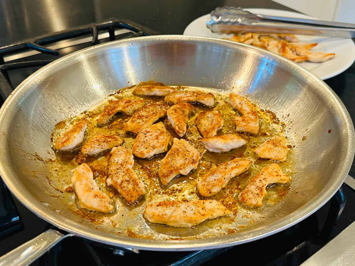 Small pieces of chicken cooking in a large steel skillet.